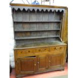 AN ANTIQUE OAK FARMHOUSE DRESSER having a three shelf canopied rack with decorative front frieze,