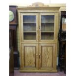 A VINTAGE STRIPPED PINE HOUSEKEEPER'S CUPBOARD with twin glazed upper doors and interior shelving