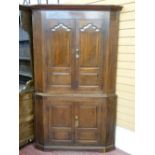 AN ANTIQUE OAK TWO PIECE STANDING CORNER CUPBOARD, twin upper and lower doors having shaped and