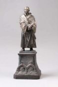 Skulptur.Spritzguss. Vollplatische Figur von Luther auf rechteckigem Sockel mit Portraits von