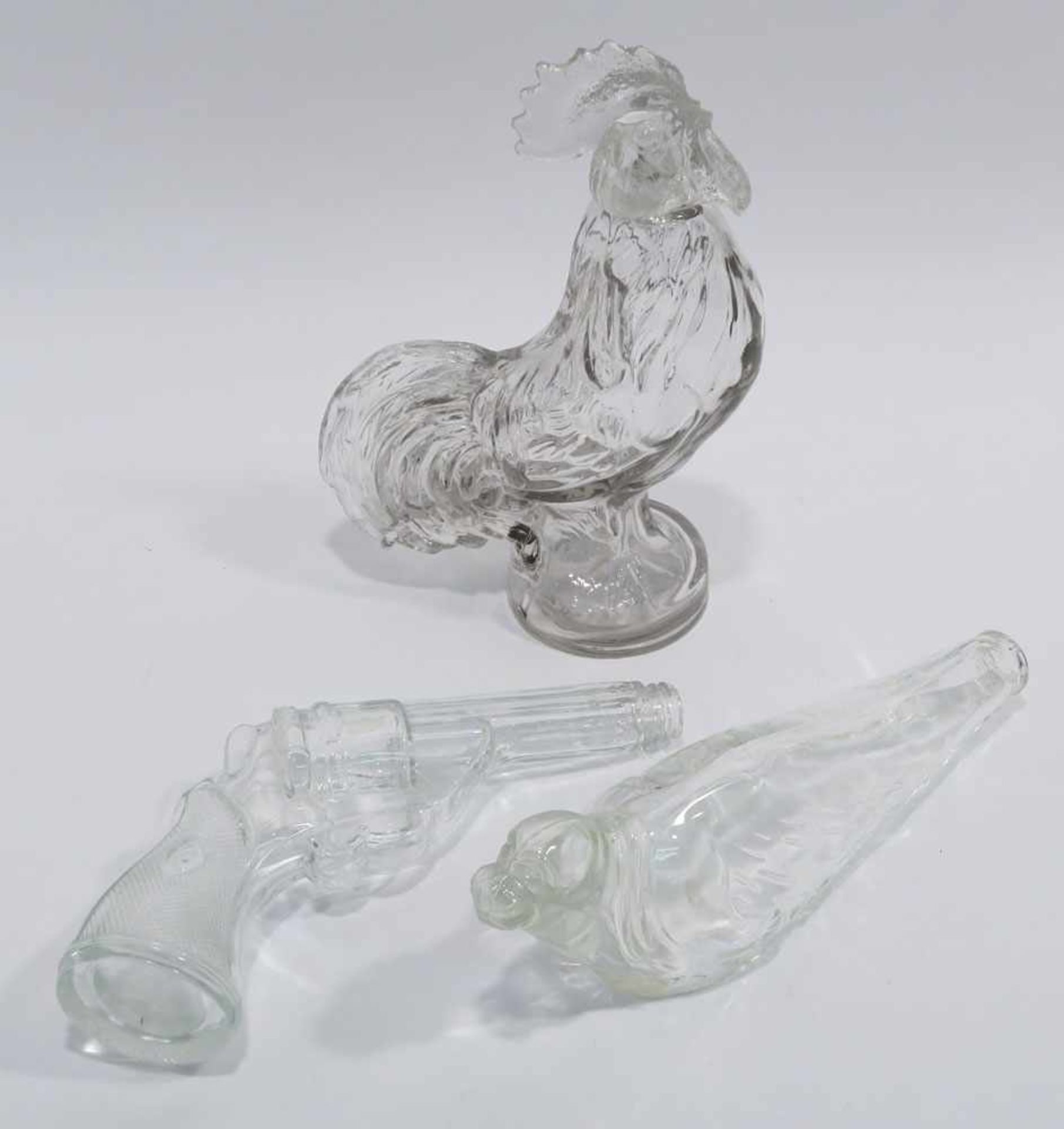 Drei Flaschen: Hahn / Pistole / RobbeFarbloses Pressglas. Tlw. best. H. 26 cm bzw. L. 26 cm und 27