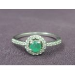 A lady's dress ring having an emerald style stone within a diamond chip surround to diamond set