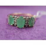 A lady's dress ring having three emeralds interspersed by diamond chips on a 9ct gold loop, size M