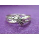 A 9ct white gold band ring with diamond chip set cross over knot decoration, size N