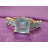 A lady's dress ring having a princess cut blue topaz style stone with set shoulders on a 9ct gold