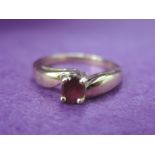 A lady's dress ring having a ruby solitaire to raised cross over shoulders on a 9ct gold loop,