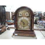 An early 20th century mahogany mantel clock having arch top with brass finials and feet, with
