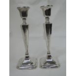 A pair of silver candlesticks having shaped tapered columns with engraved scroll decoration to