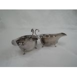 A pair of silver sauce boats of plain form having shaped rims, loop handles and trefoil hoof feet,