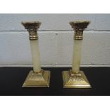 A pair of Regency style brass and onyx column candlesticks having corinthian inspired decoration