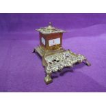 A vintage brass cast ink well with ornate decoration and ceramic inner fitment