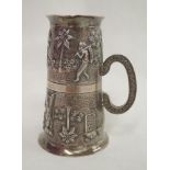 An Indian silver double spirit measure having repousse country scene decoration and moulded handle