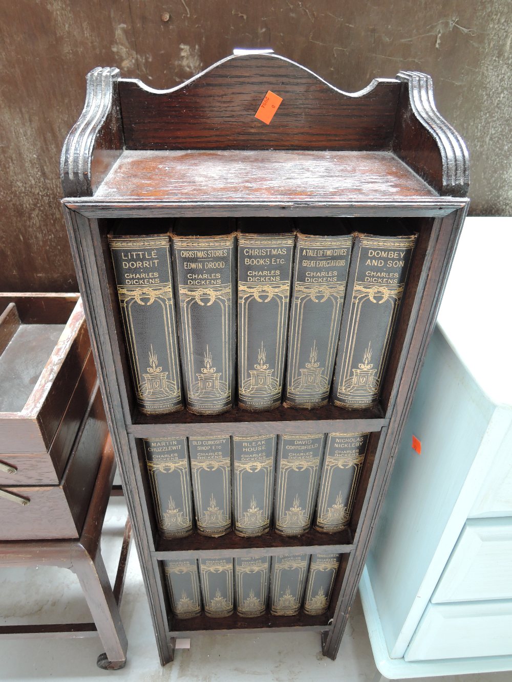 A small dark oak bookshelf with Charles Dickens volumes included