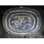 A large blue and white willow ware style charger plate