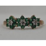 A lady's dress ring having three small emerald and diamond daisy clusters in a raised claw mount