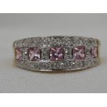 A lady's dress ring having a central row of pink gem stones bordered by diamond chips on an 18ct