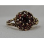 A lady's dress ring having a garnet cluster in a claw set basket mount with curled shoulders on a