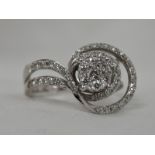 A lady's dress ring having a diamond cluster within stylised open swirl diamond set shoulders on a