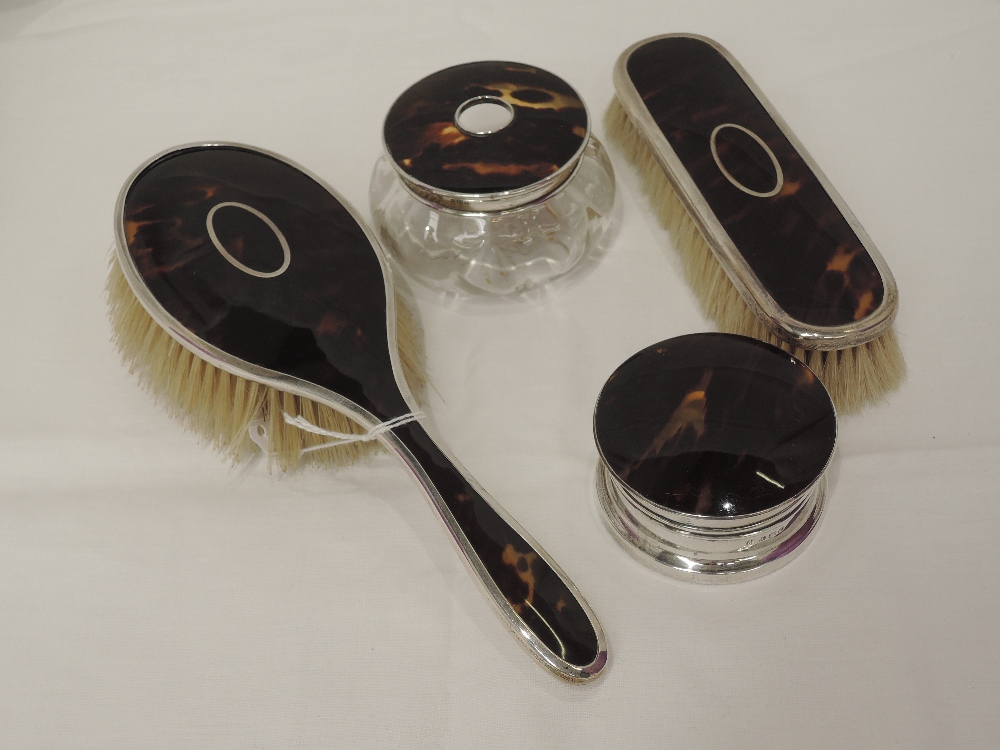 Four HM silver and tortoise shell dressing table items including two brushes, a glass pot with