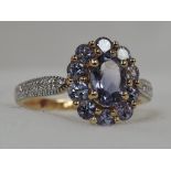 A lady's dress ring having tanzanite style oval cluster to diamond chip set shoulders on an 18ct