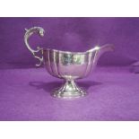 An Edwardian sauce boat of facetted oval form with reeded rim, pedestal foot and moulded scroll