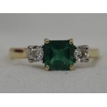 A lady's dress ring having a central step cut emerald, approx 0.5ct flanked by two brilliant cut