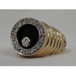 A gents yellow metal signet ring stamped 14K having a circular onyx panel with floating diamond