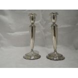 A pair of Edwardian silver candle sticks of plain tapered urn form to weighted circular bases,