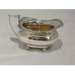 A silver cream jug of oval form having a gadrooned rim, an acanthus leaf handle and bun feet,