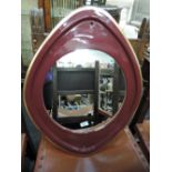 A ceramic framed eye shaped mirror with art deco design and burgundy finish