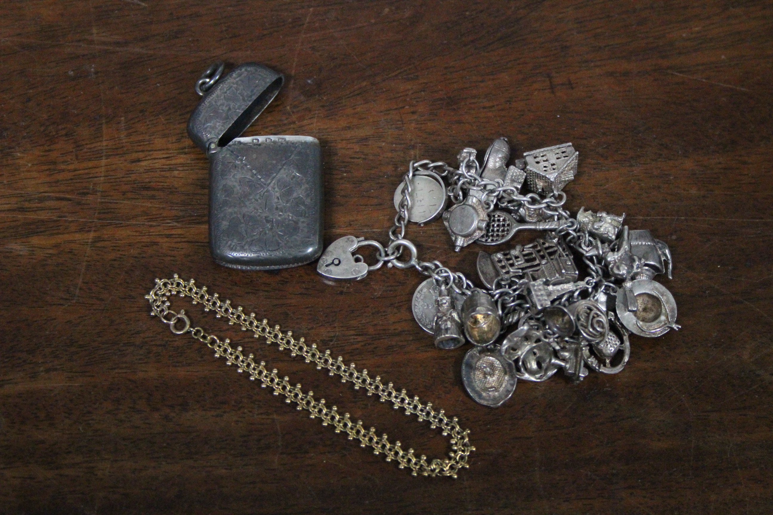 A silver engraved Vesta case; a white-metal charm bracelet; a yellow-metal child’s bracelet &