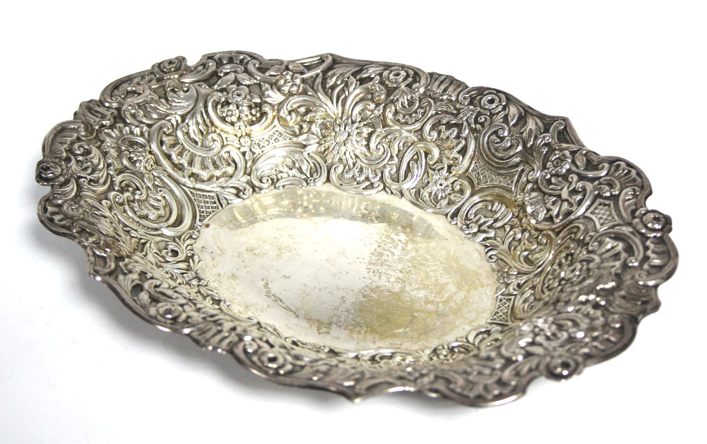 An Edwardian oval shallow dish, the wide borders embossed with flowers & scrolls, 10” x 7½”;