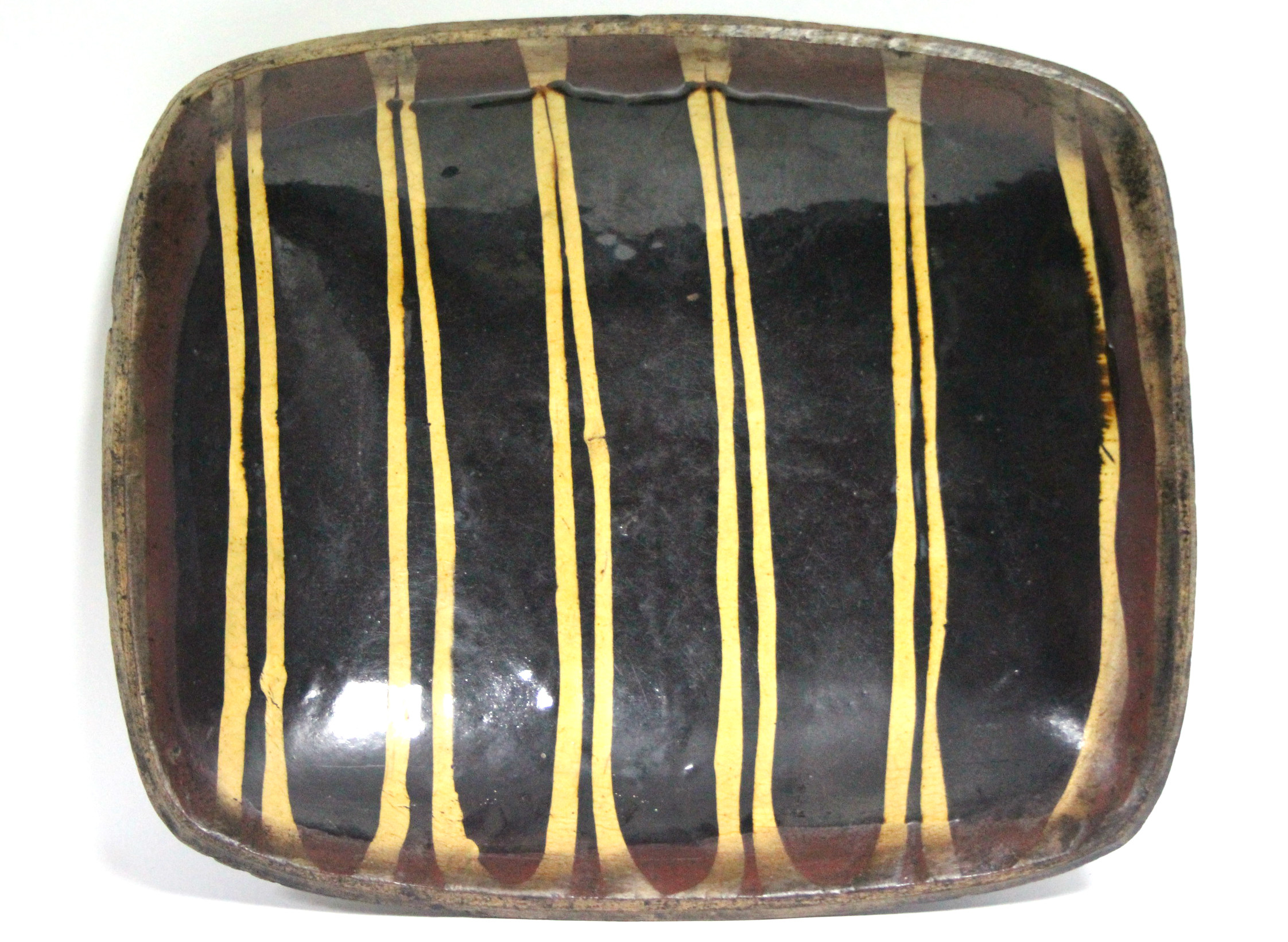 A rectangular slipware dish decorated with pairs of cream lines on a chocolate-brown ground; 15” x