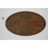 A reproduction cast-iron oval sign "ANTIQUES", 8¼" x 13½".