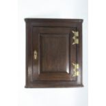 An 18th century oak hanging corner cupboard, fitted two shelves enclosed by bevelled panel door with