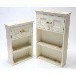 Two white painted wooden wall cabinets, each enclosed by pair of panel doors above an open shelf,