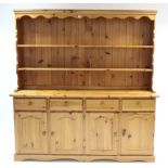 A pine large dresser, the upper part fitted two open shelves & with panelled back, the base fitted
