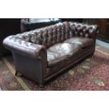 A Chesterfield-style buttoned deep red (dark) leather three-seater settee, on short turned legs with