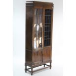 A 1930’s oak tall standing bookcase with three adjustable shelves enclosed by pair of leaded