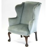A MID-18th century WING-BACK ARMCHAIR upholstered pale blue velour, with scroll arms, & on carved