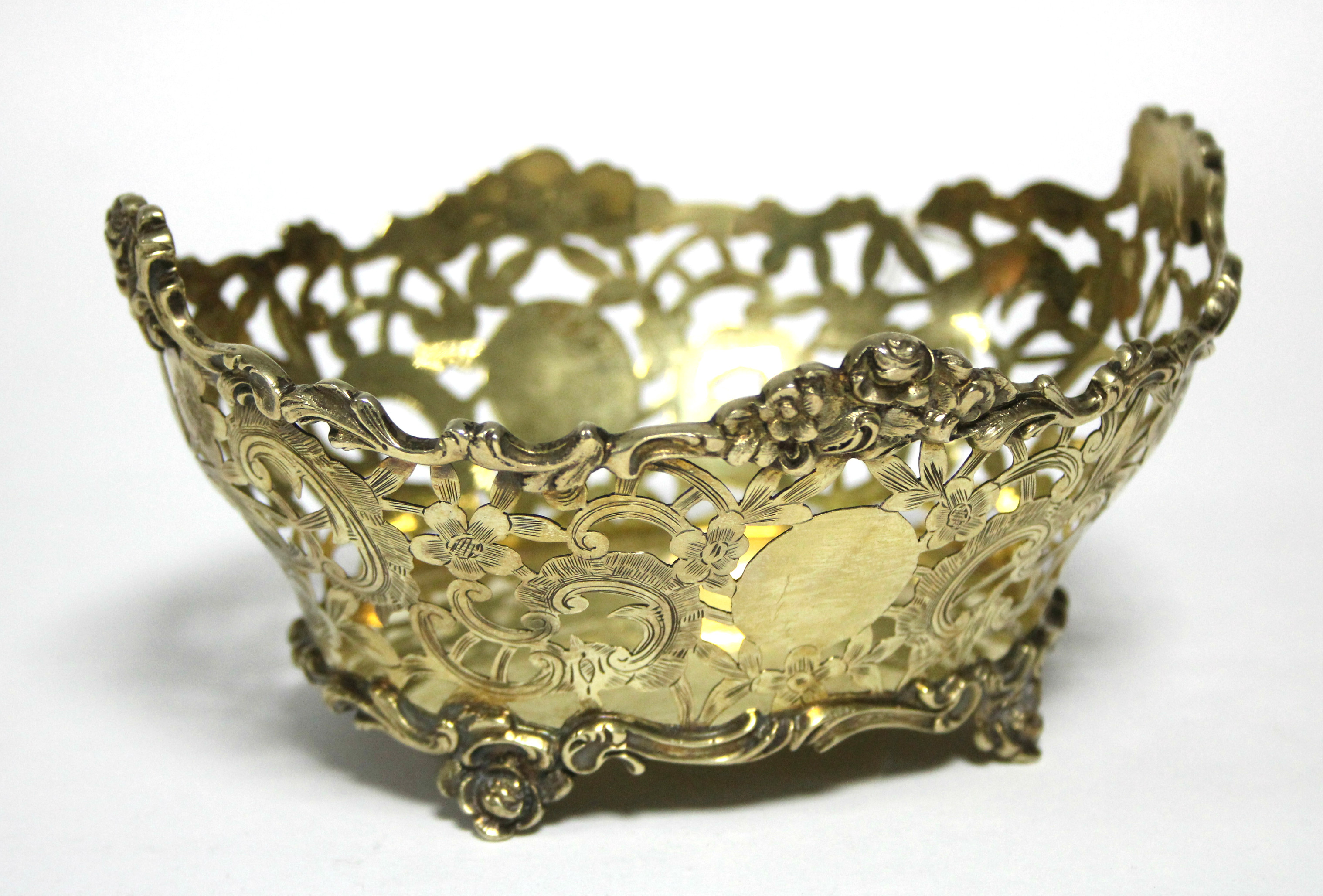 An Edwardian silver-gilt pierced oval dish with shaped cast scroll rim & feet, & engraved flower &