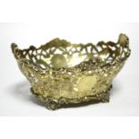 An Edwardian silver-gilt pierced oval dish with shaped cast scroll rim & feet, & engraved flower &