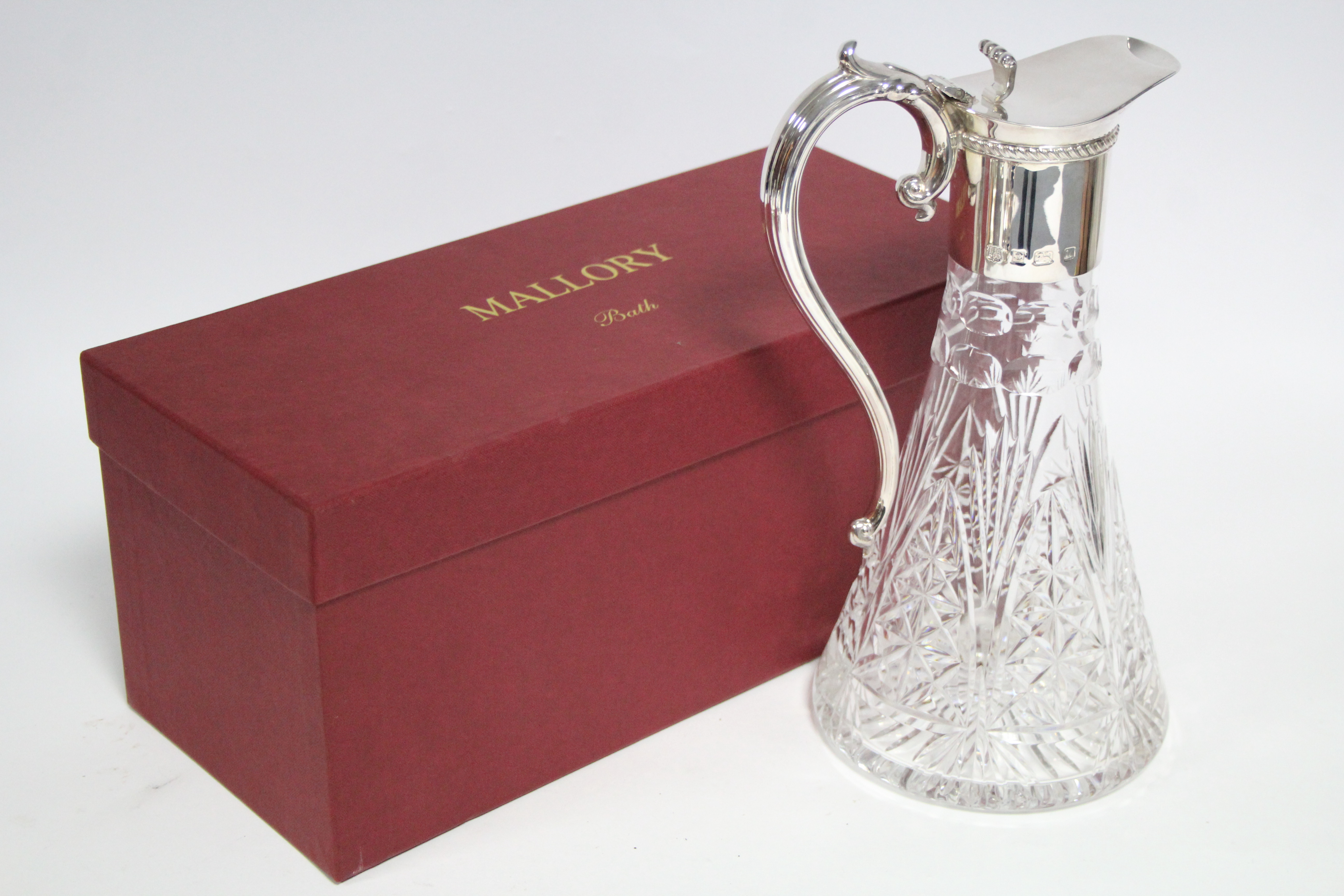 A modern cut glass claret jug of round tapered form, with silver neck-mount, hinged lid, & scroll