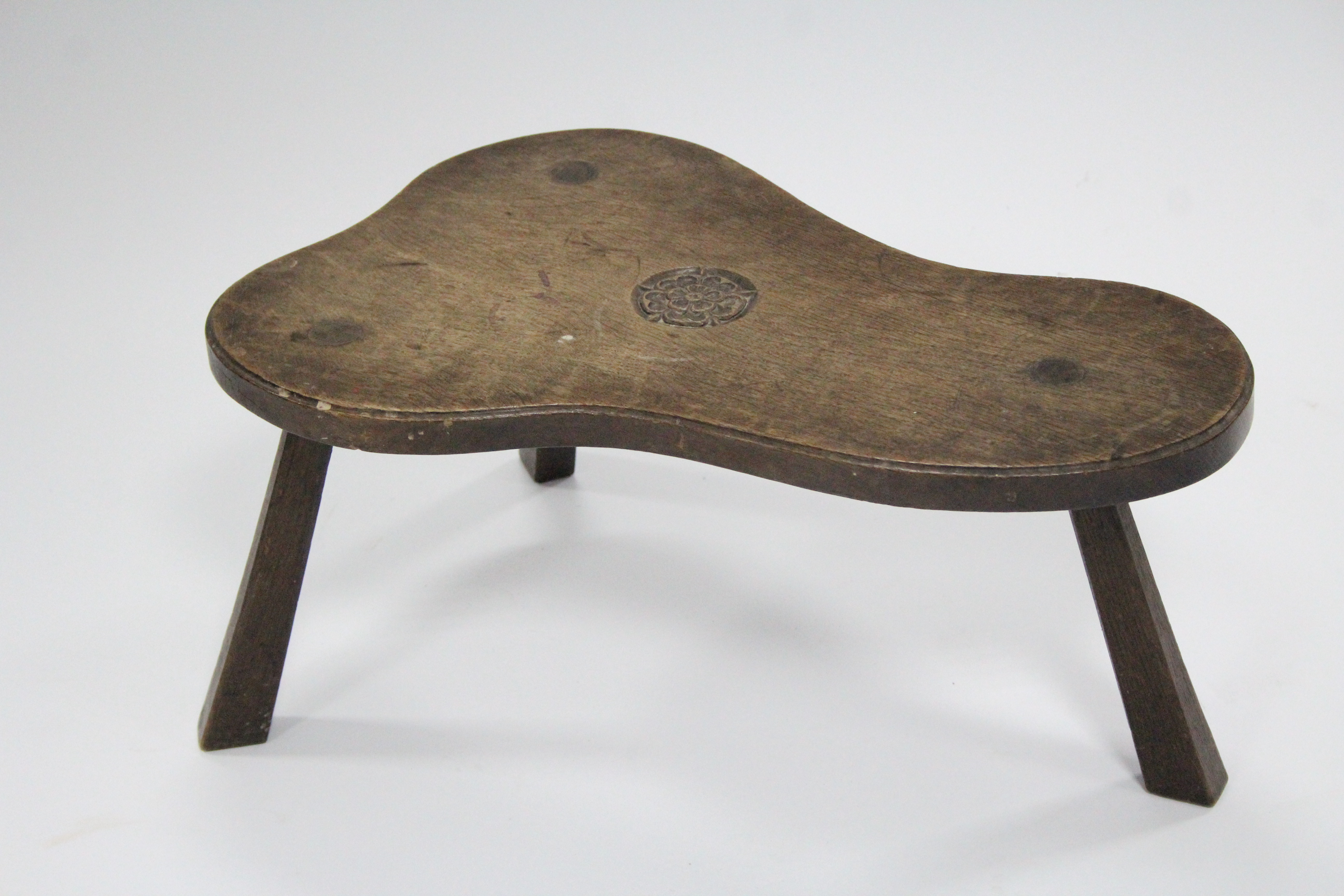 An oak milking stool by JACK GRIMBLE, the shaped seat with carved Tudor rose, on three chamfered