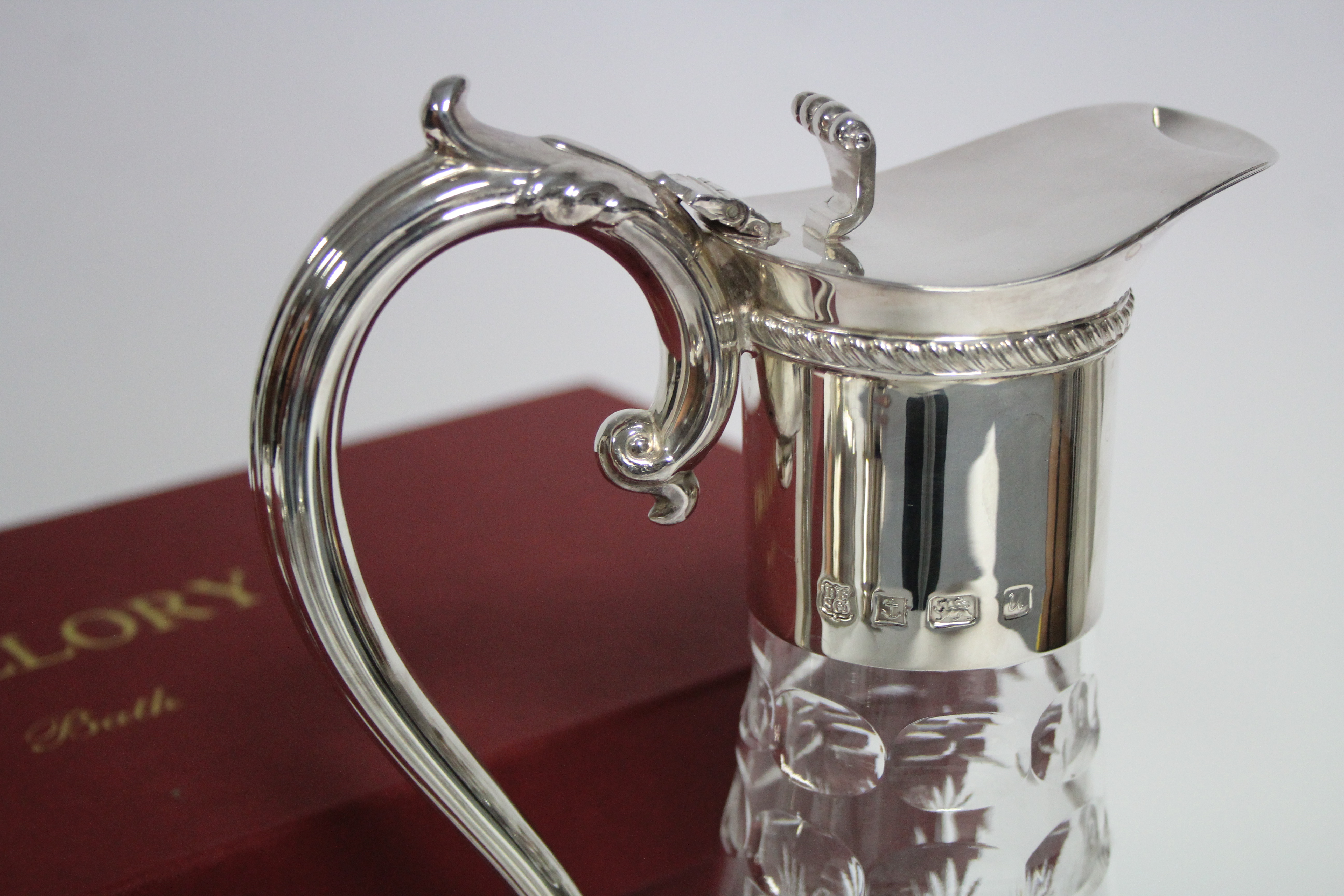 A modern cut glass claret jug of round tapered form, with silver neck-mount, hinged lid, & scroll - Image 2 of 2