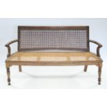 A late 19th century Indian teak settle with woven cane back & seat, curved open arms, & on turned