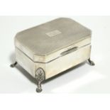A George V rectangular trinket box with canted corners & engine-turned hinged lid, on four foliate