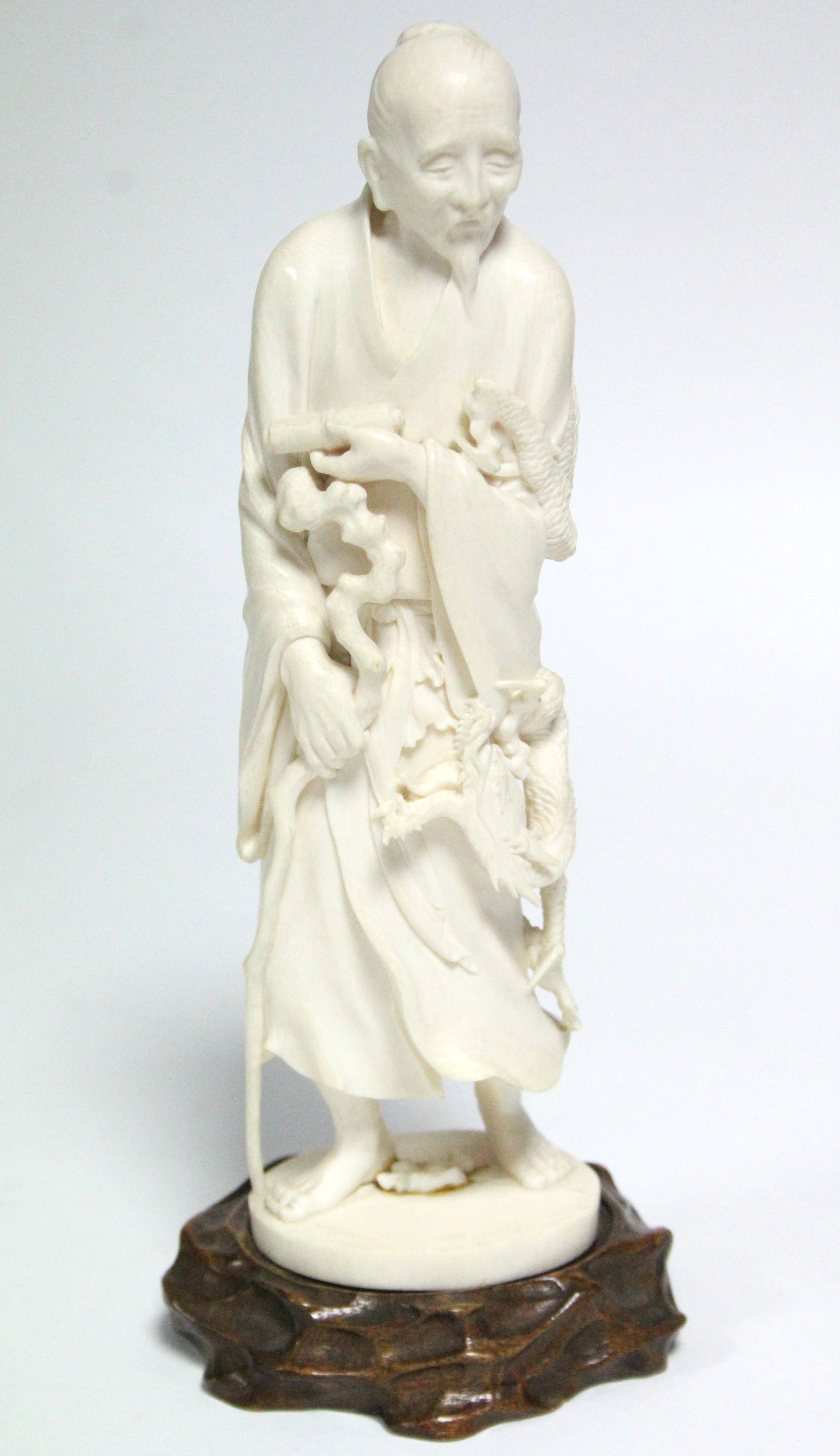 A late 19th century Japanese ivory okimono of a standing male scholar holding a scroll & a staff,