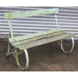 A late 19th/early 20th century green painted teak & wrought-iron garden bench on scroll-shaped end