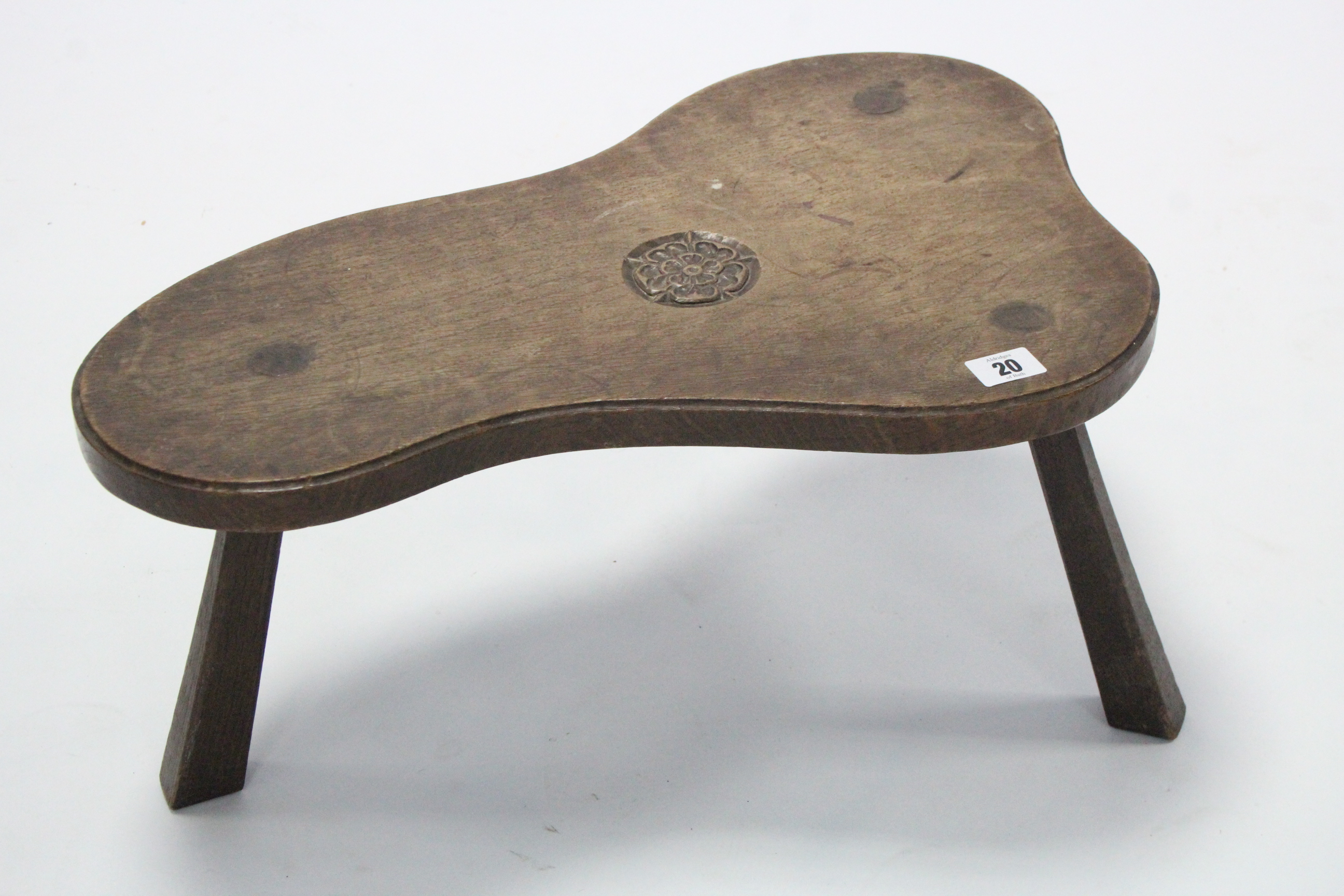 An oak milking stool by JACK GRIMBLE, the shaped seat with carved Tudor rose, on three chamfered